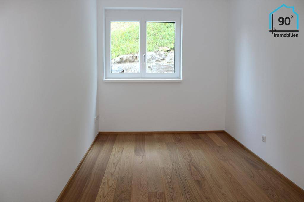 Helles Zimmer mit Holzboden und Fenster mit Blick ins Grüne.