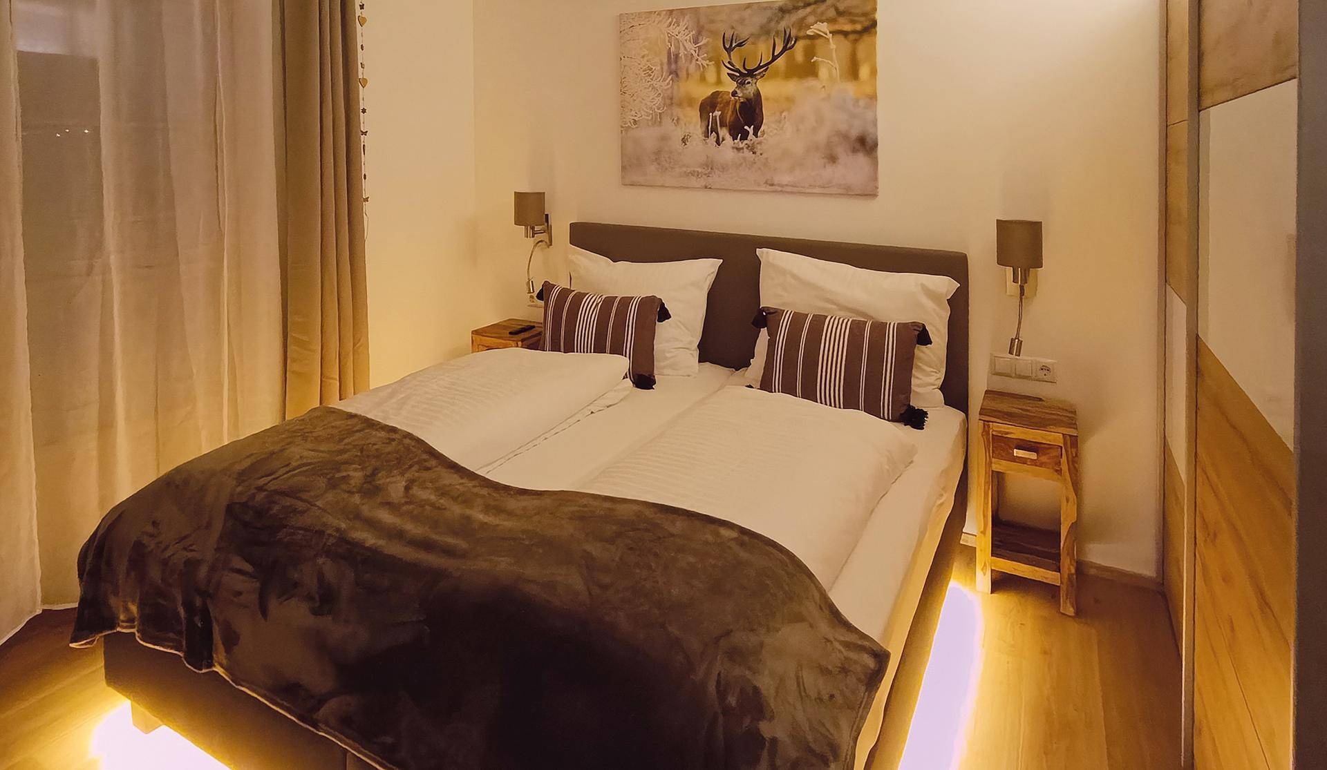 Gemütliches Schlafzimmer mit Doppelbett, indirekter Beleuchtung und Holzelementen im alpinen Stil.