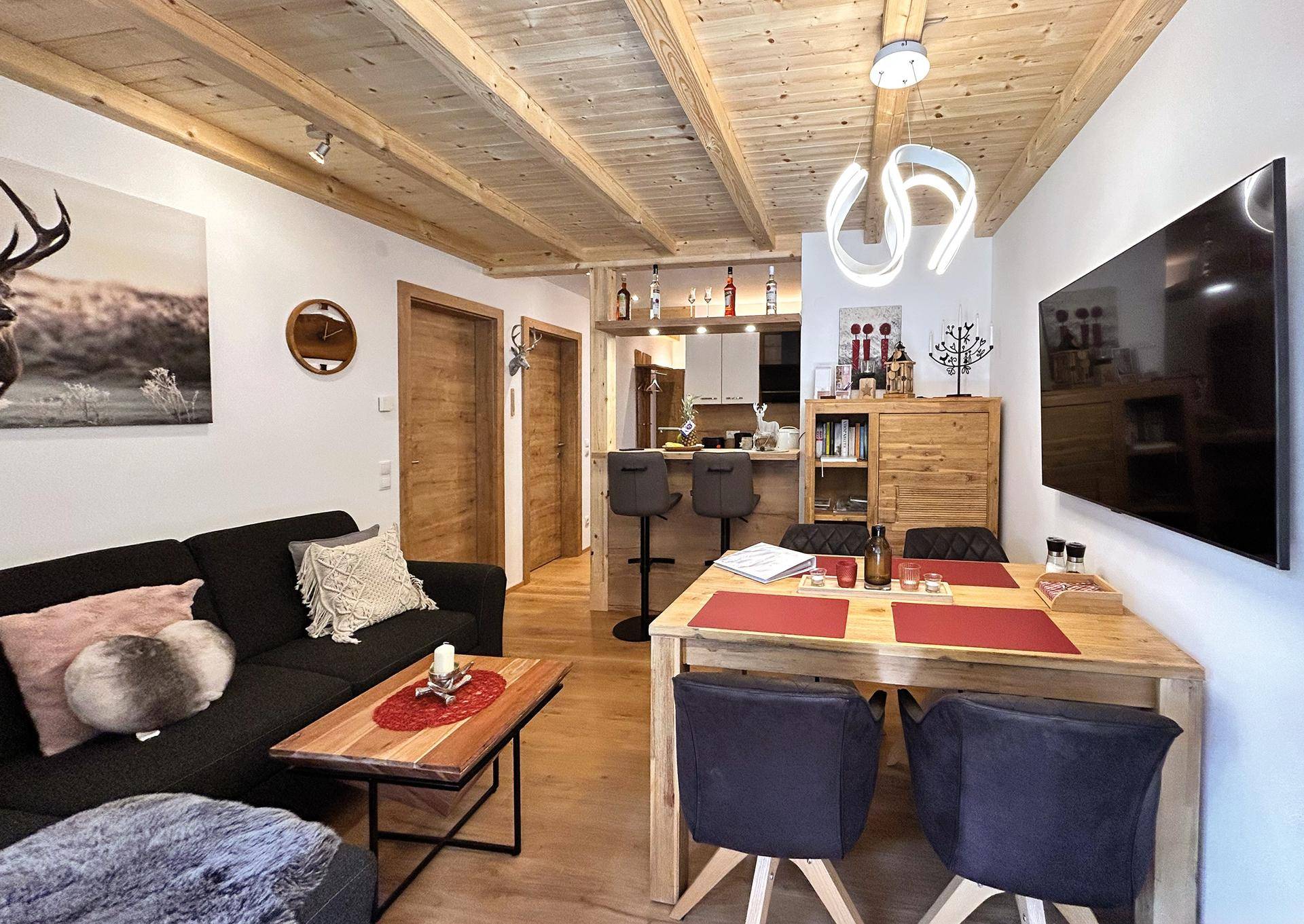 Offener Wohn- und Essbereich mit Holzbalkendecke, modernem Lichtdesign und integrierter Küchenzeile.