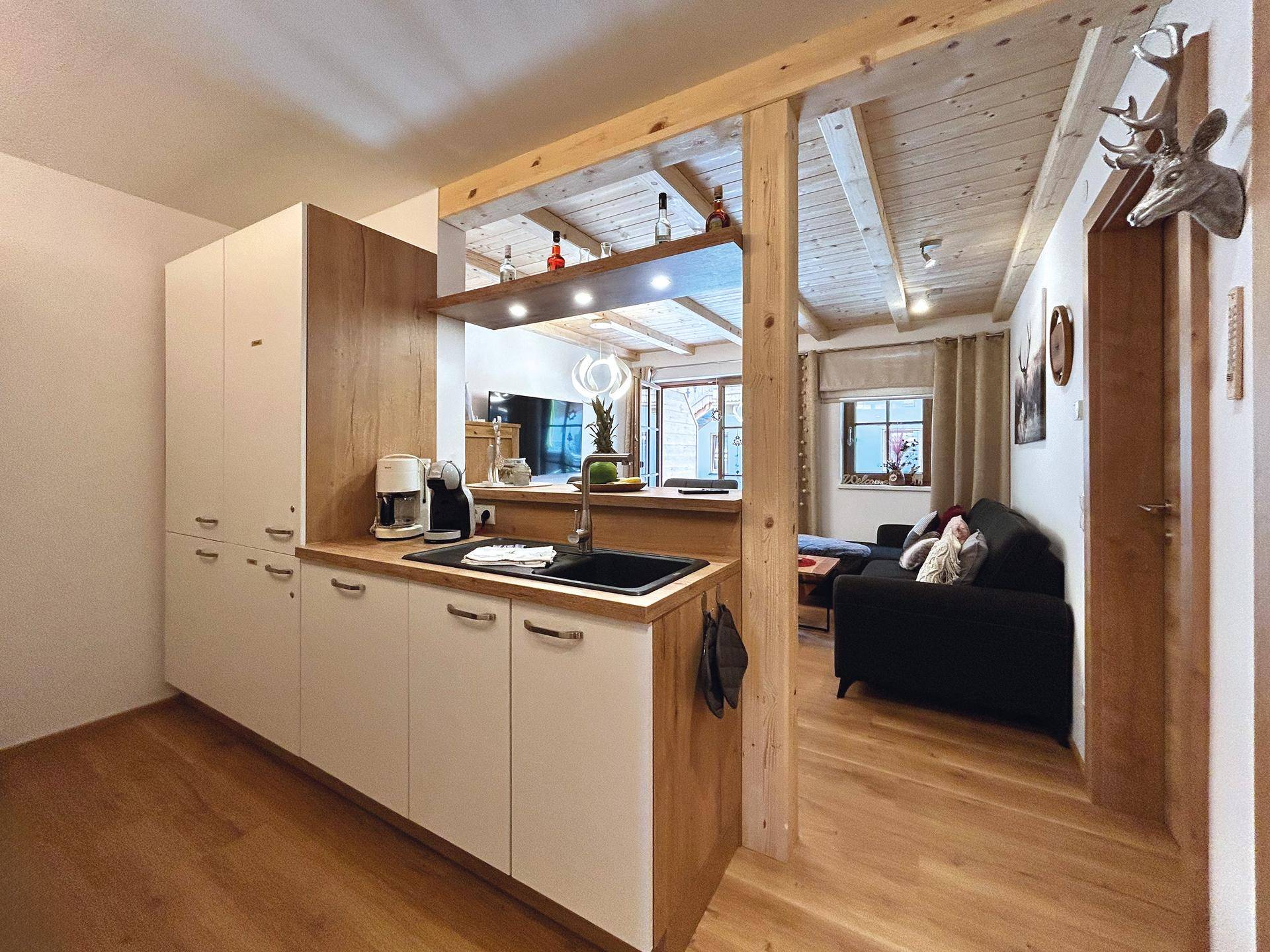 Kompakte Küchenzeile mit Holz- und weißen Fronten, offen zum Wohnbereich und Holzbalkendecke.