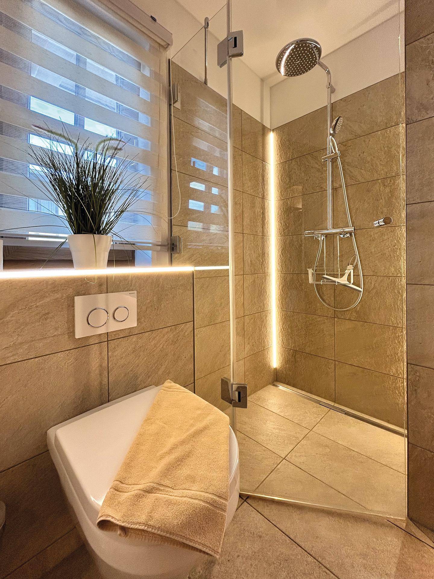 Modernes Badezimmer mit begehbarer Dusche, großen Fliesen und einem Fenster für natürliches Licht.