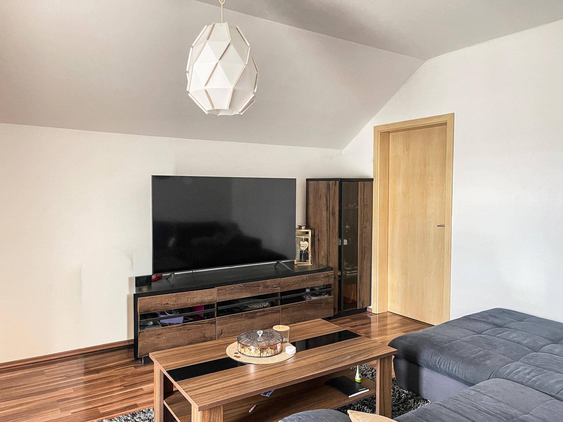 Heller Wohnbereich mit großem Fernseher, Medienmöbeln und Dachschräge.