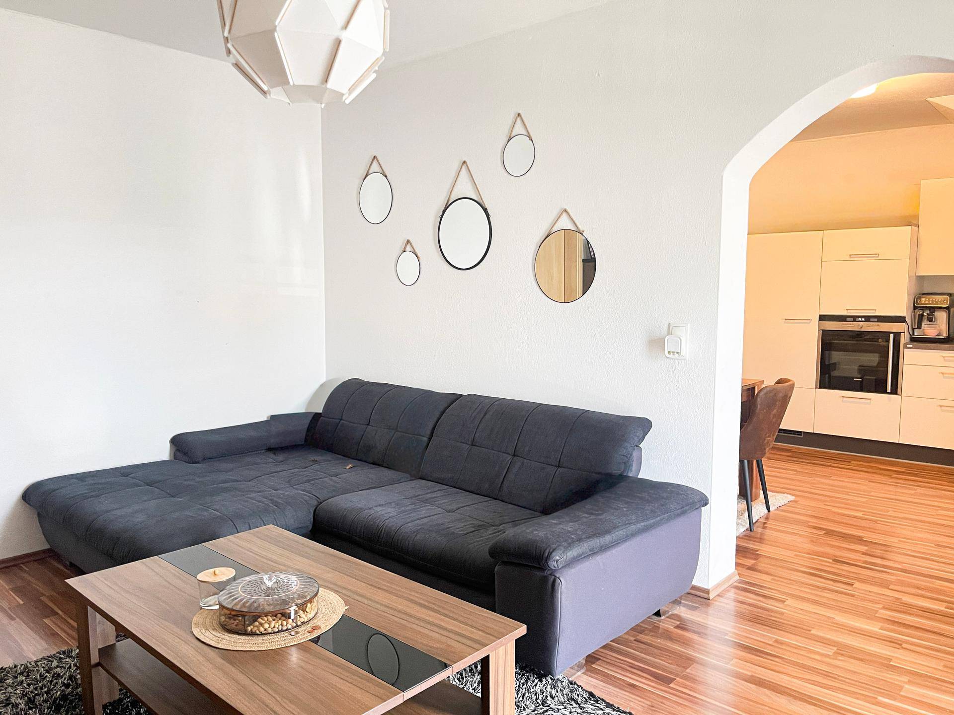 Gemütliches Wohnzimmer mit dunklem Sofa, Holztisch und offener Verbindung zur Küche.