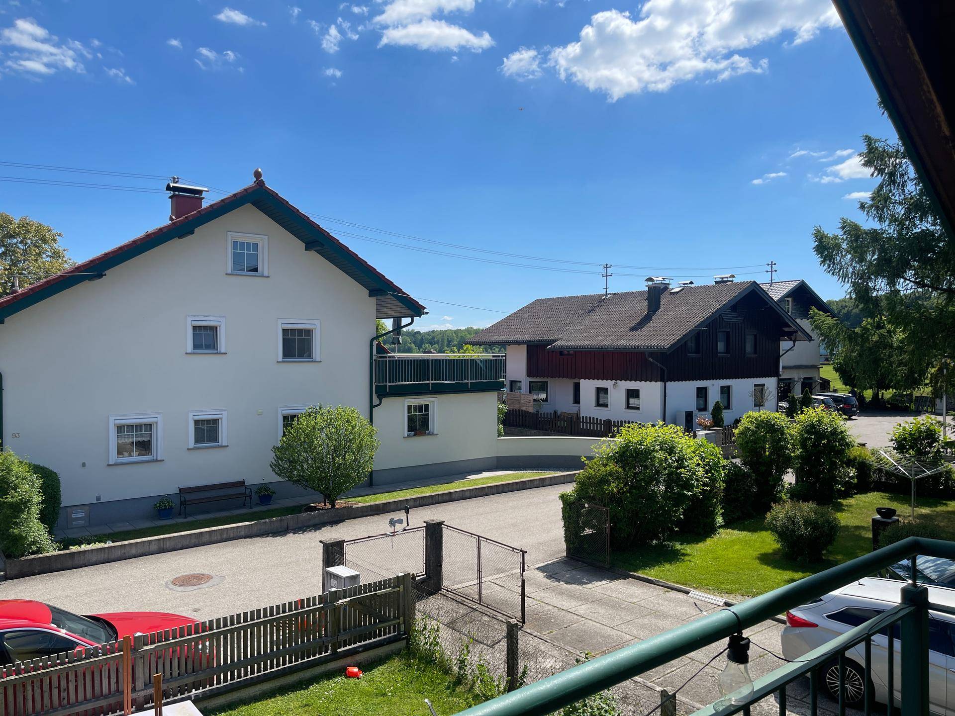 Blick von einem Balkon auf die umliegende Wohngegend mit weiteren Häusern und viel Grün.