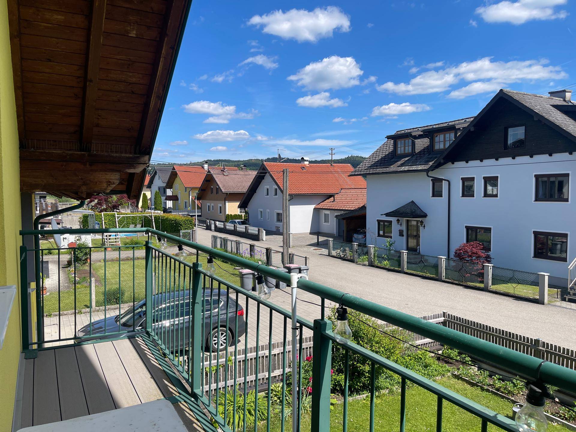 Sonniger Balkon mit Holzboden und Blick auf die ruhige Wohnstraße und Nachbarhäuser.