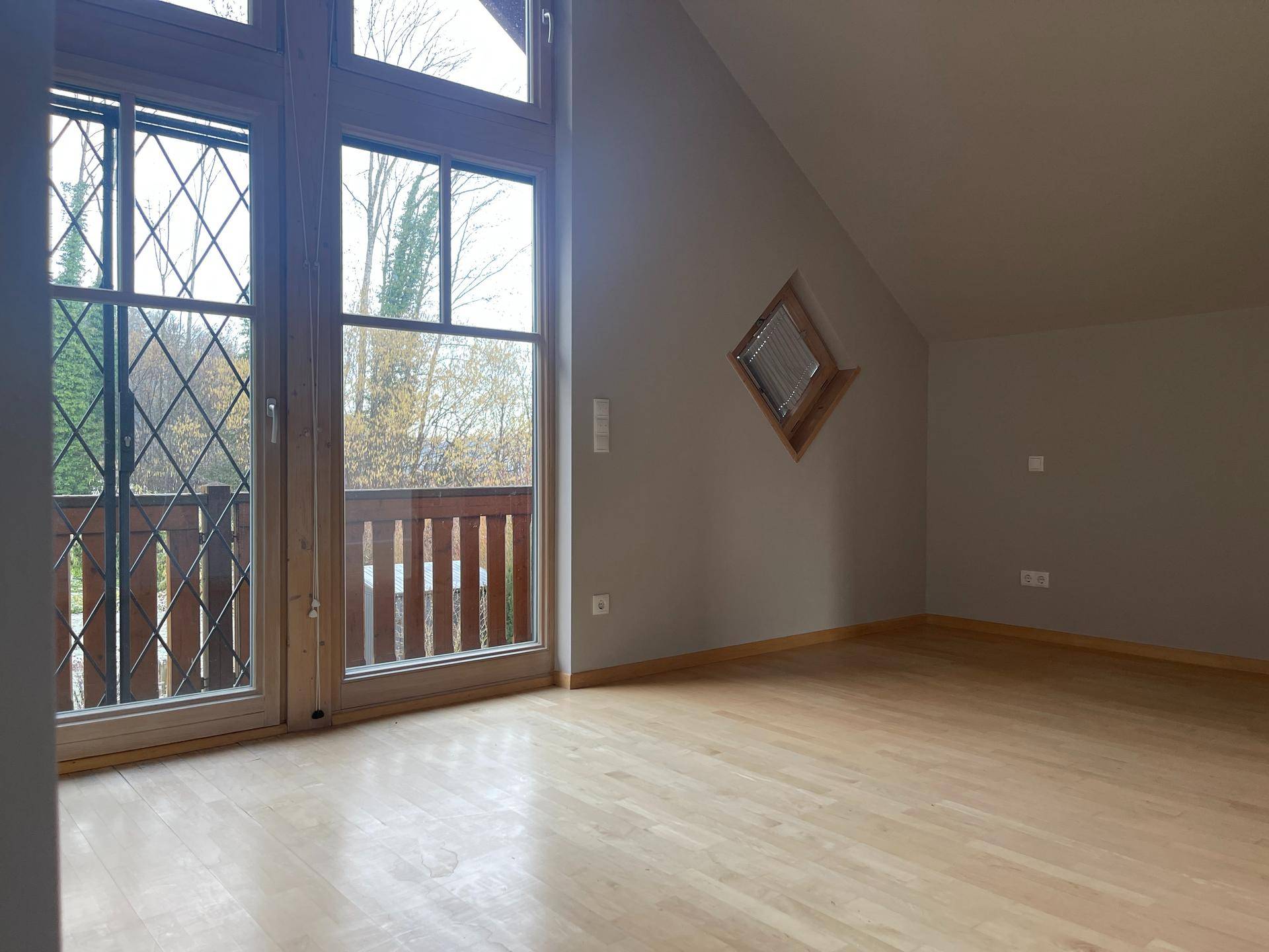 Geräumiges Schlafzimmer mit Holzboden, Zugang zum Balkon und Dachschräge, hell und einladend.