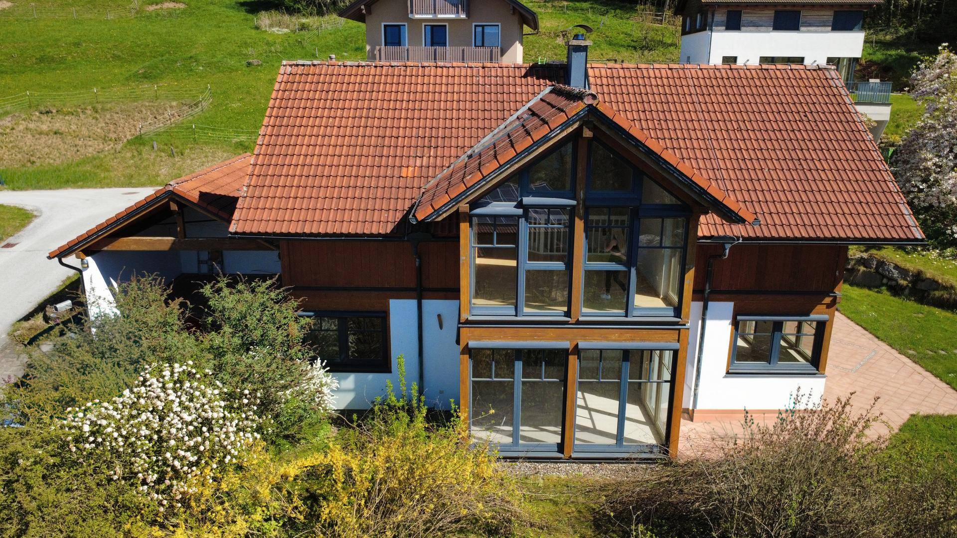 Ansicht des Hauses mit großen Glasfronten und traditionellem Ziegeldach in grüner Umgebung.