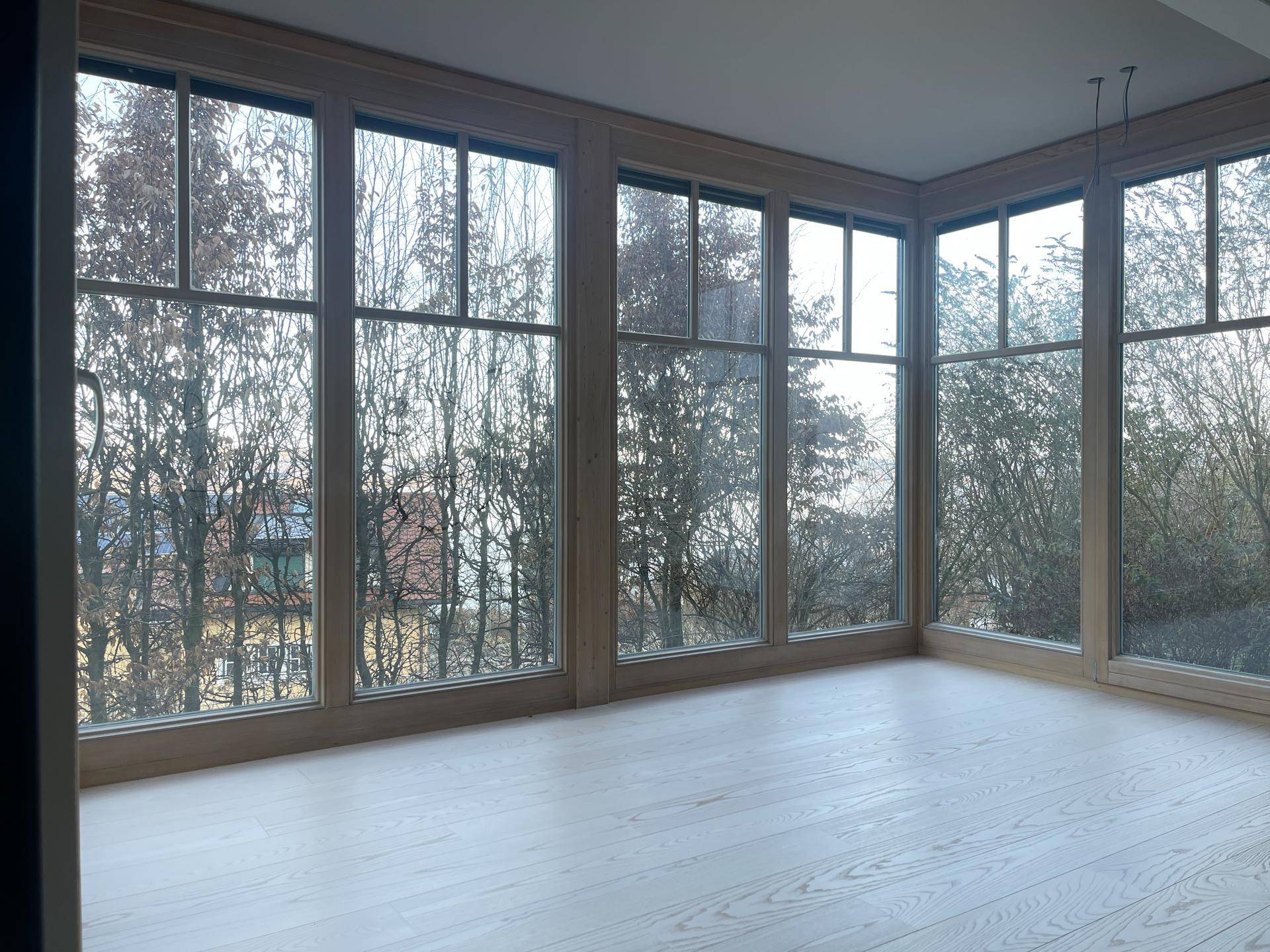 Heller Innenraum mit großen Fenstern und hellem Holzboden, bietet viel natürliches Licht und Ausblick.