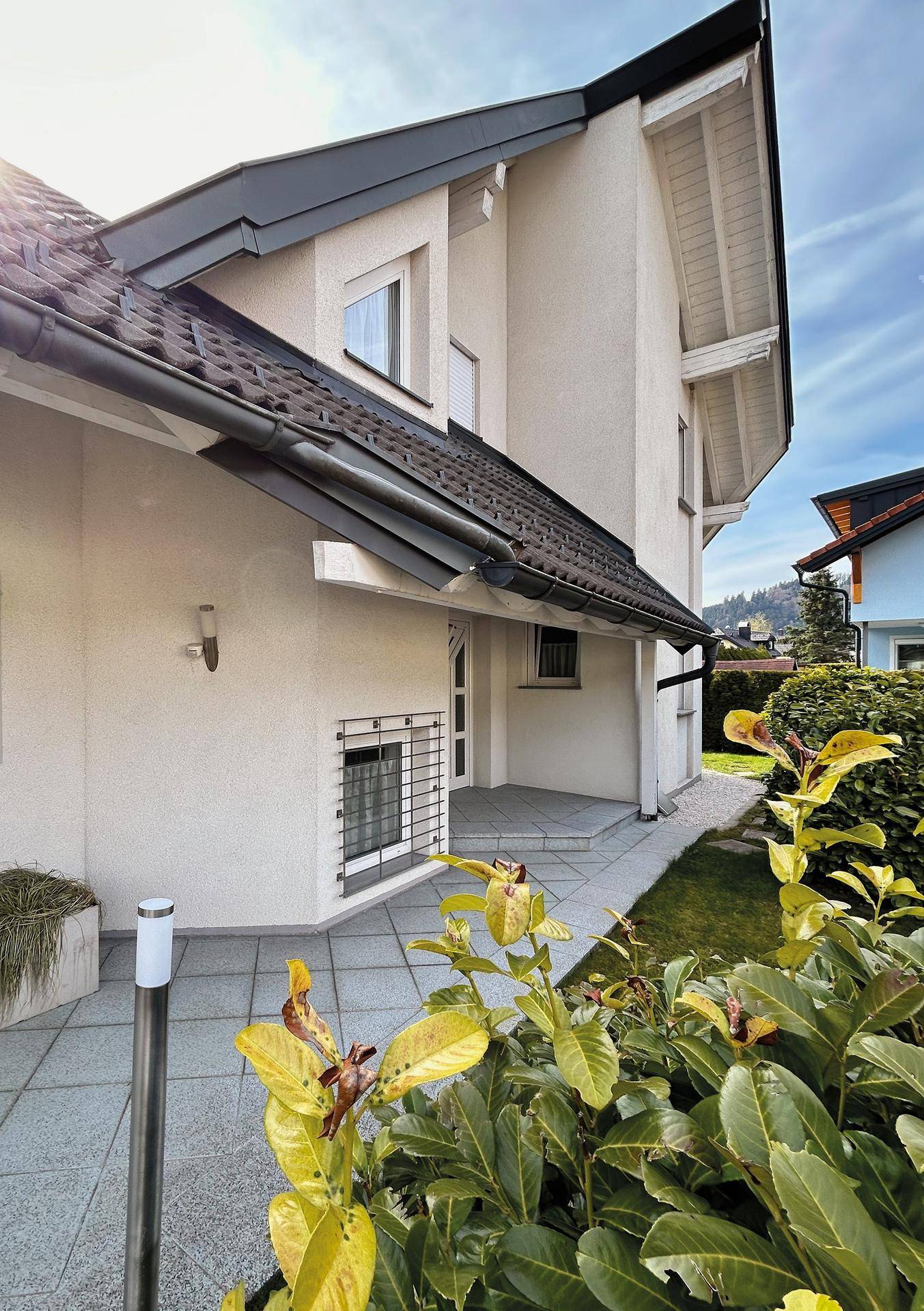 Moderne Hausfassade mit Satteldach, gepflegtem Garten und Zugang zum Eingangsbereich.