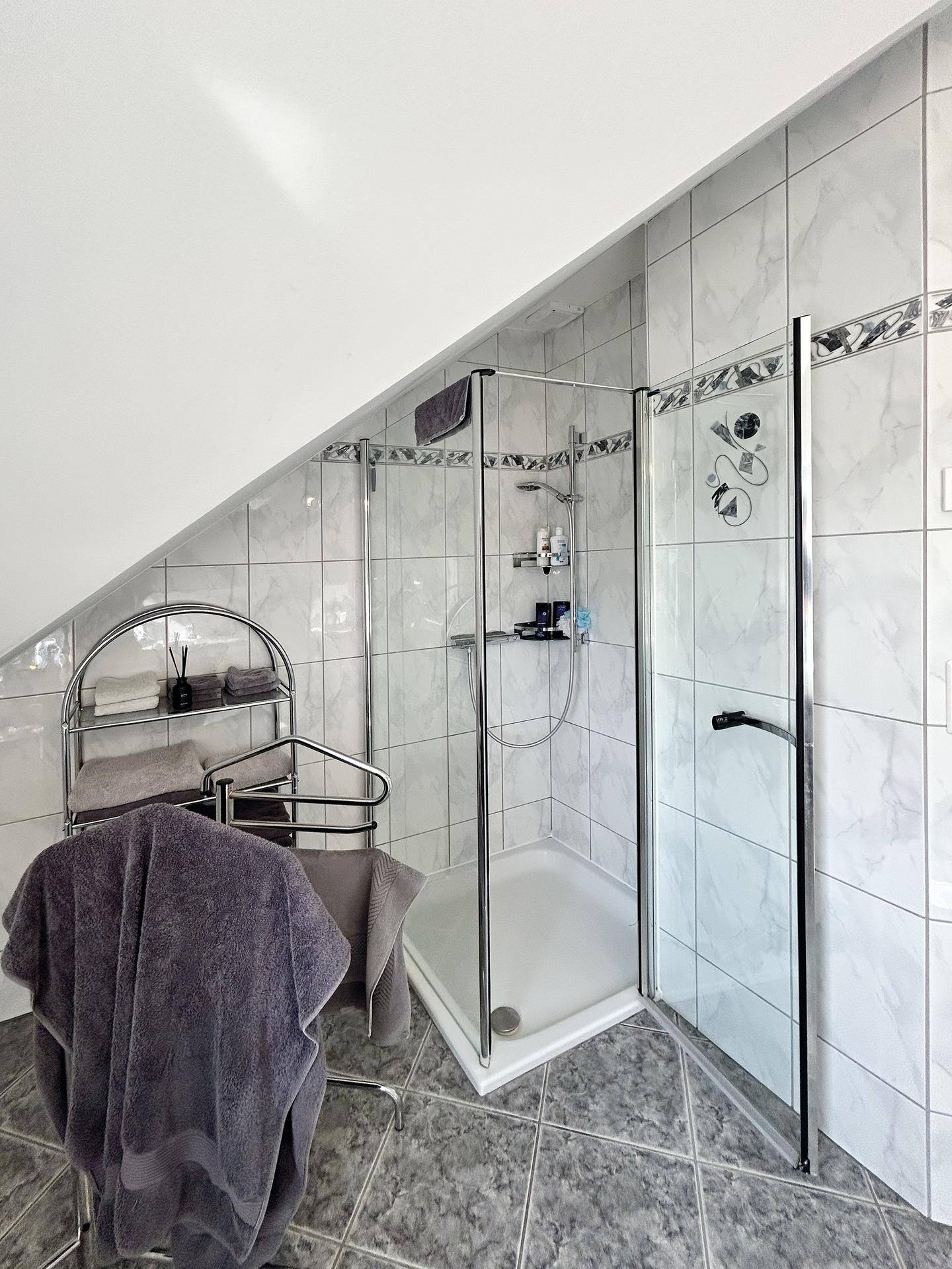 Helles Badezimmer im Dachgeschoss mit Duschkabine und modernen Fliesen.