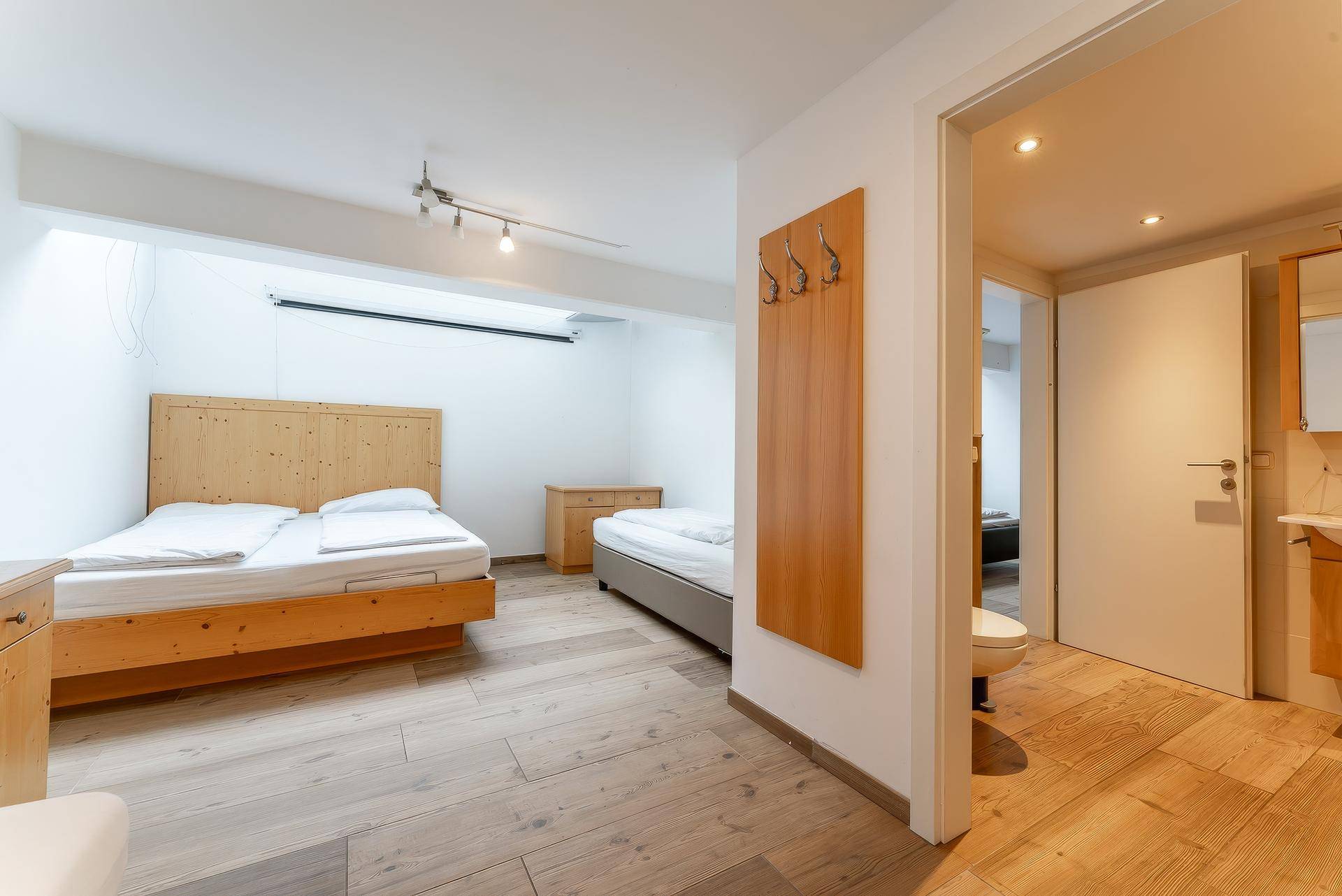 Helles Schlafzimmer mit zwei Einzelbetten, Holzboden und Zugang zu einem WC.