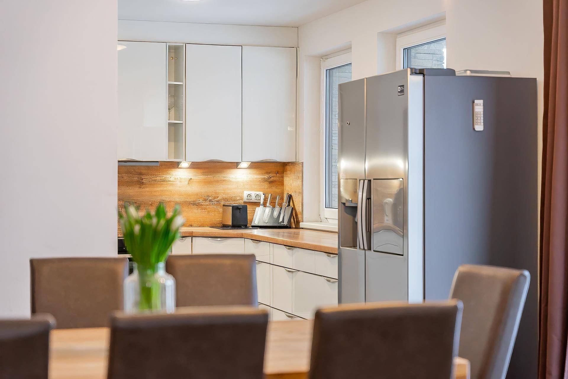 Moderne Küche mit hellen Schränken, Holzakzenten und einem großen Kühlschrank.
