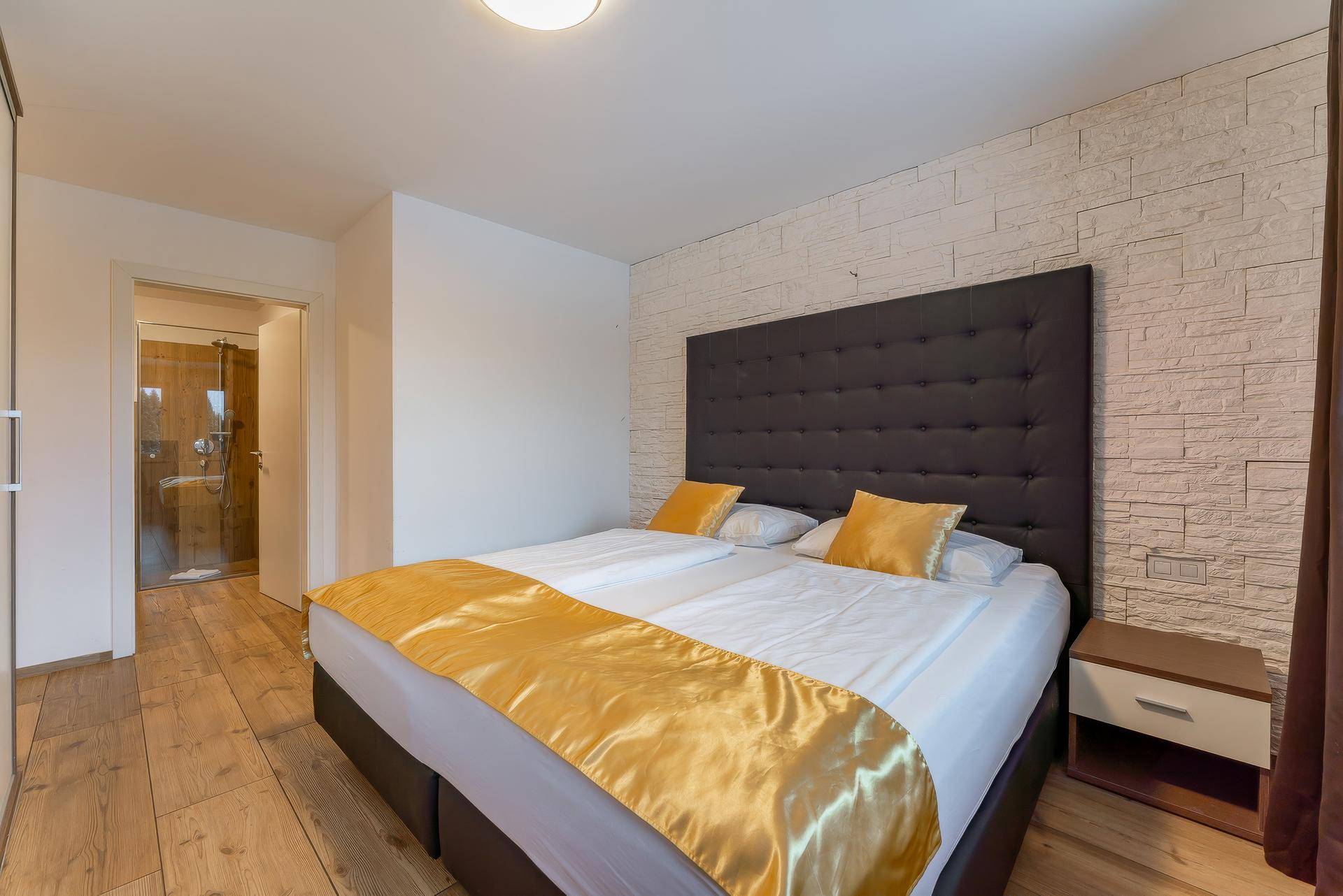 Gemütliches Schlafzimmer mit Doppelbett, Holzboden und Zugang zu einem Badezimmer.