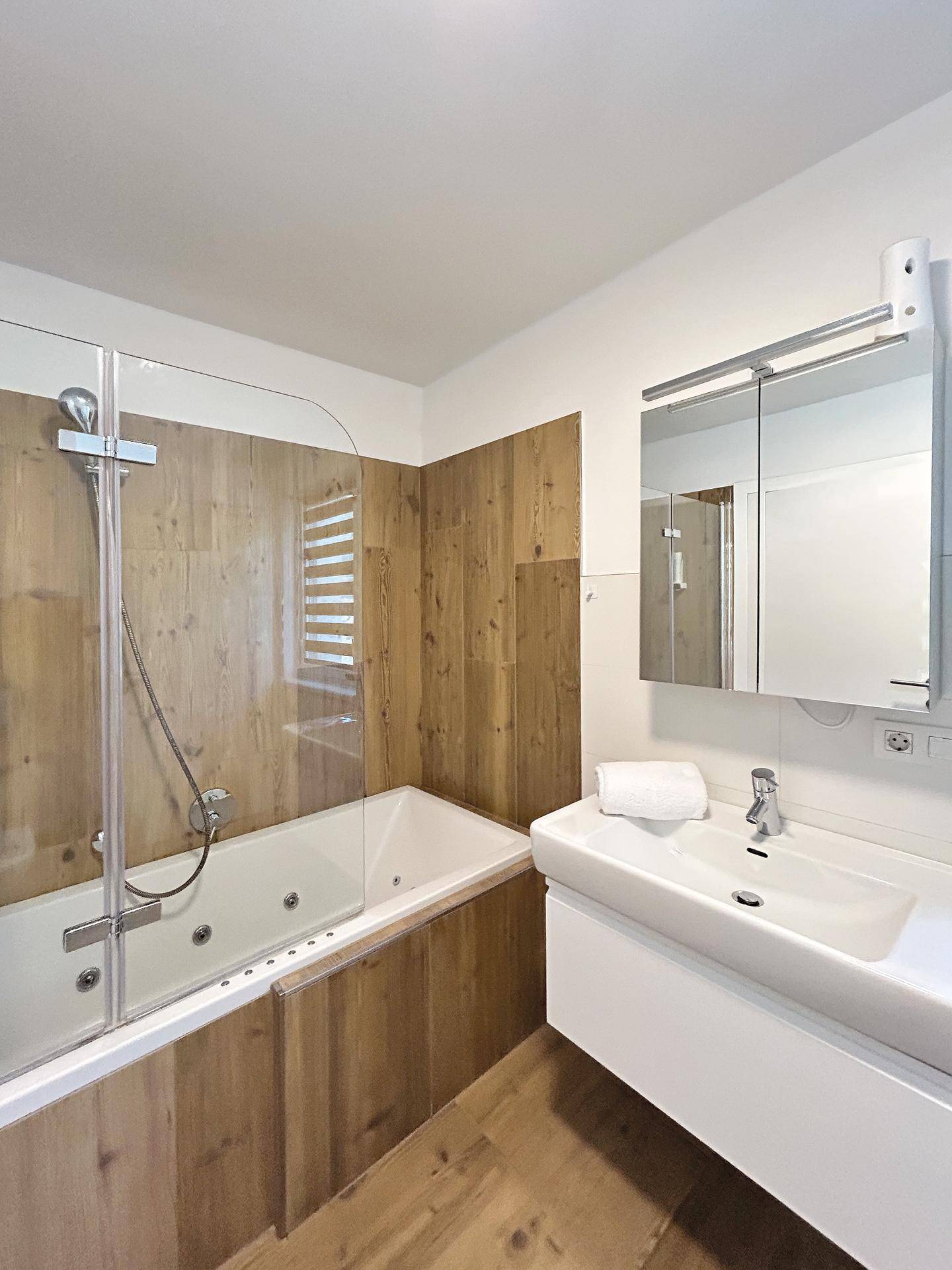 Modernes Badezimmer mit Badewanne, Duschfunktion und Holzverkleidung an den Wänden.
