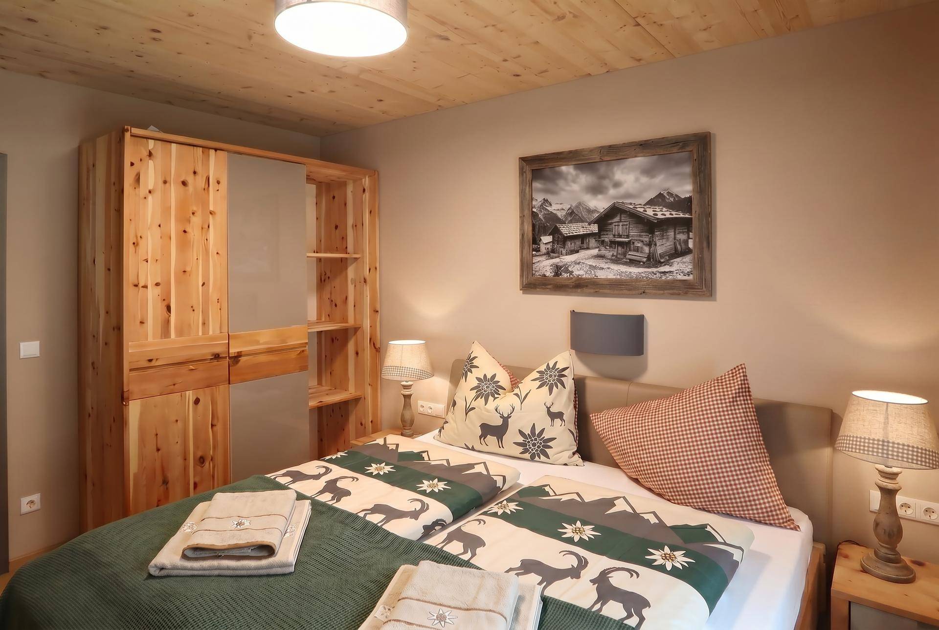 Gemütliches Schlafzimmer mit Doppelbett, Holzschrank und alpiner Bettwäsche unter einer Holzdecke.
