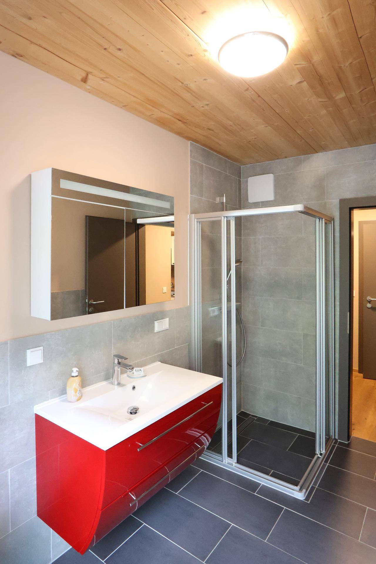 Modernes Badezimmer mit rotem Waschtisch, Duschkabine und Holzdeckenverkleidung.