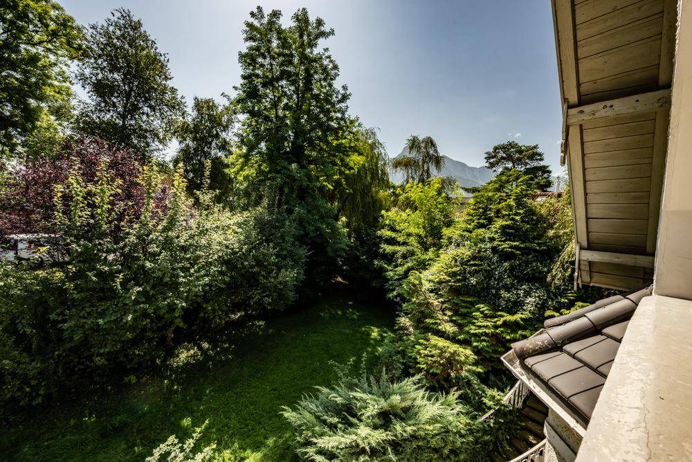 Weitläufiger Blick über den grünen Garten mit hohen Bäumen und majestätischen Bergen im Hintergrund.