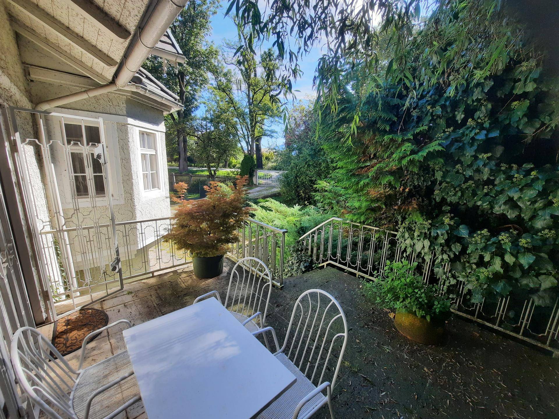 Gemütliche Terrasse mit Gartenmöbeln, umgeben von üppigem Grün und Zugang zum Garten.
