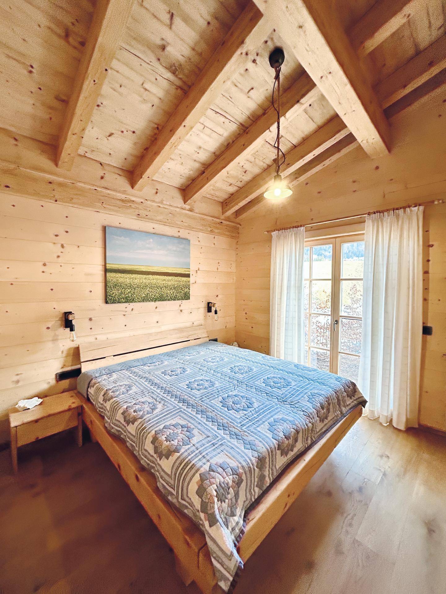 Gemütliches Schlafzimmer mit Holzwänden, Holzbalkendecke und Blick ins Grüne.