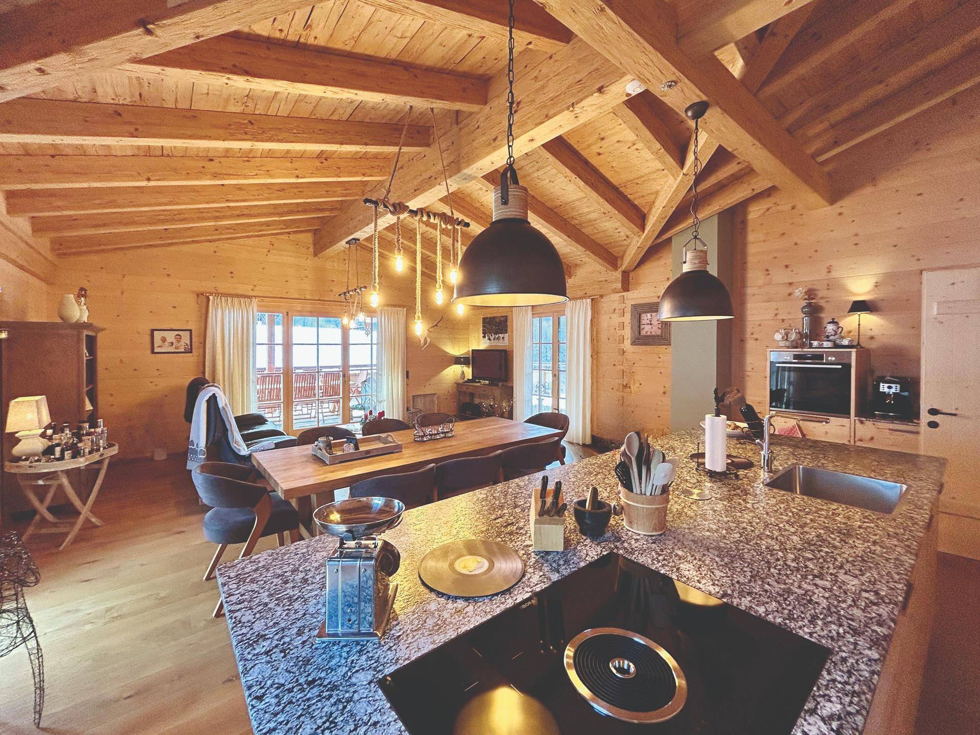 Offener Wohn- und Essbereich im Chalet-Stil mit Holzbalkendecke und moderner Küche.