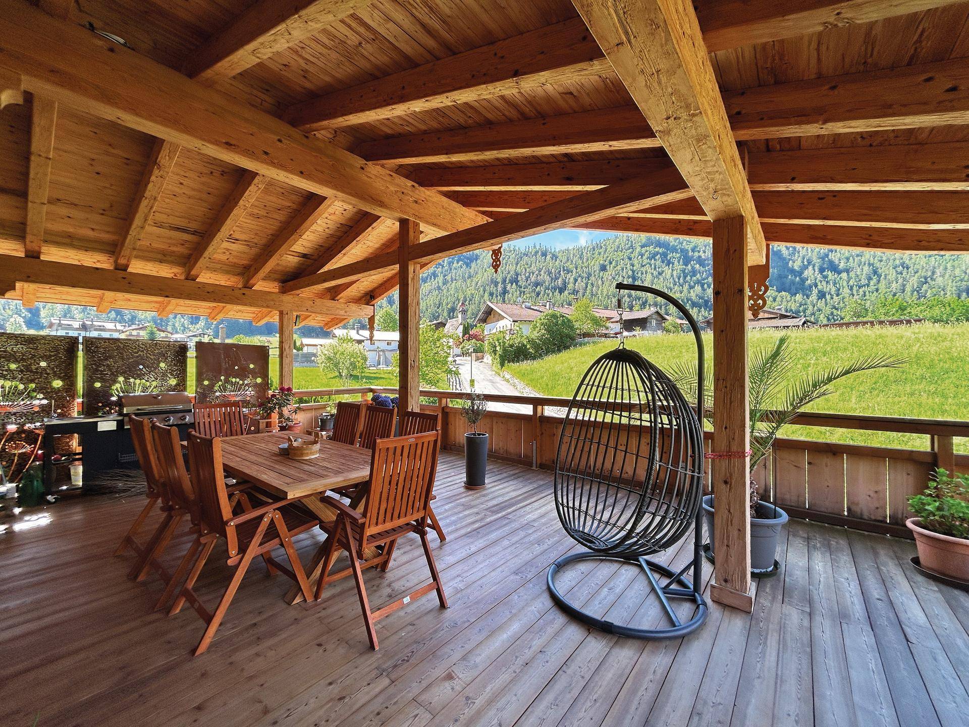 Große überdachte Holzterrasse mit Esstisch und weitem Blick auf die grüne Landschaft.