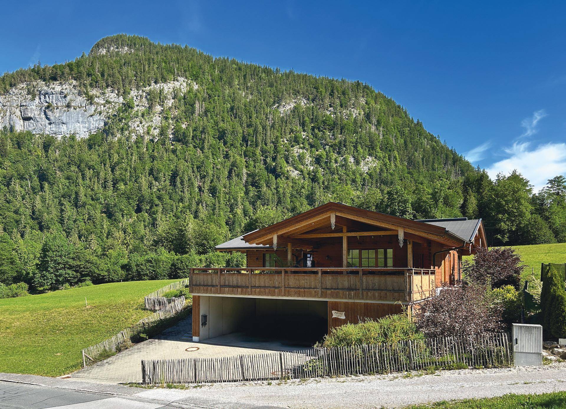 Idyllisches Holzchalet mit Balkon und Tiefgarage vor einer bewaldeten Bergkulisse.