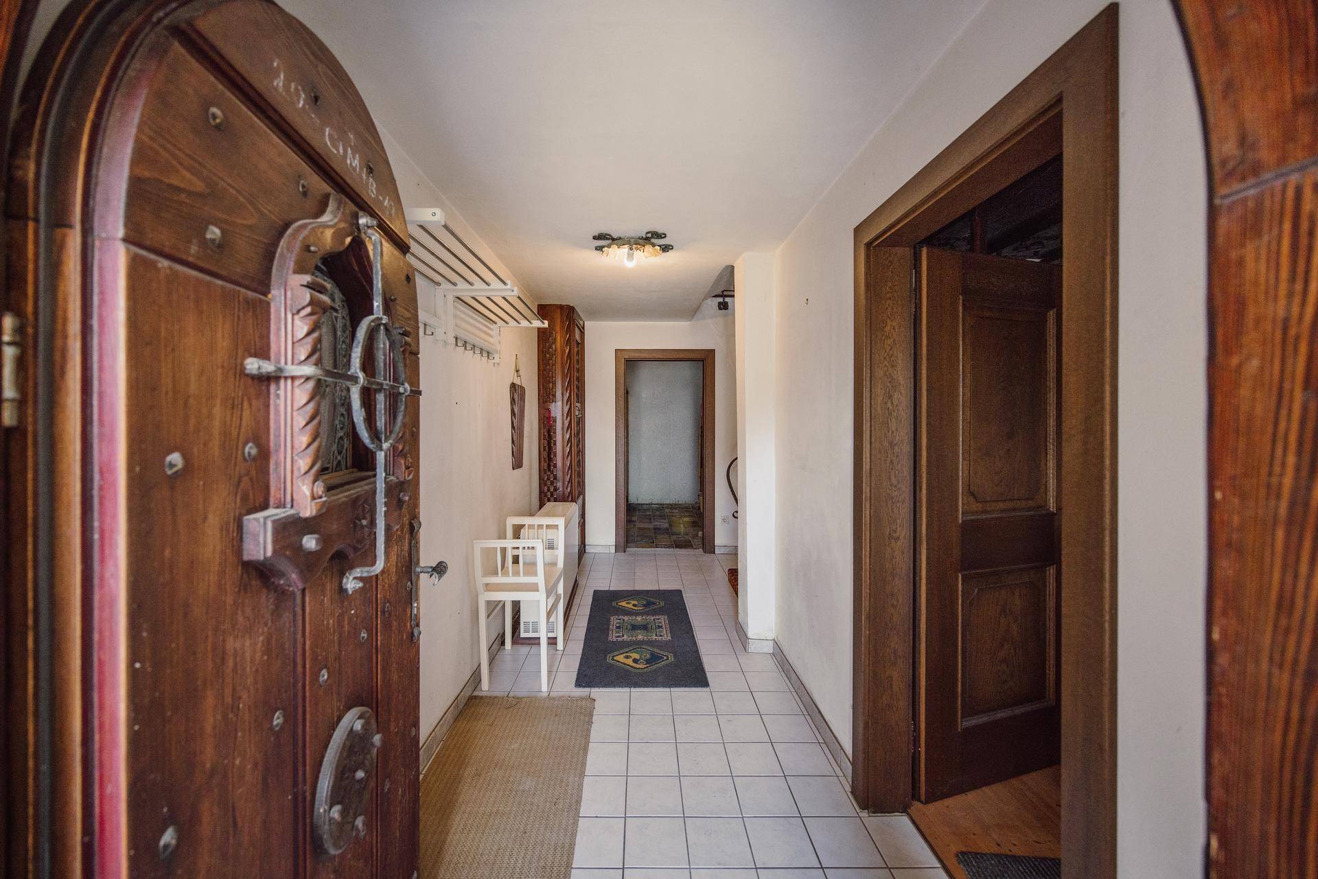 Traditioneller Eingangsbereich mit geschnitzter Holztür, Fliesenboden und Garderobe.
