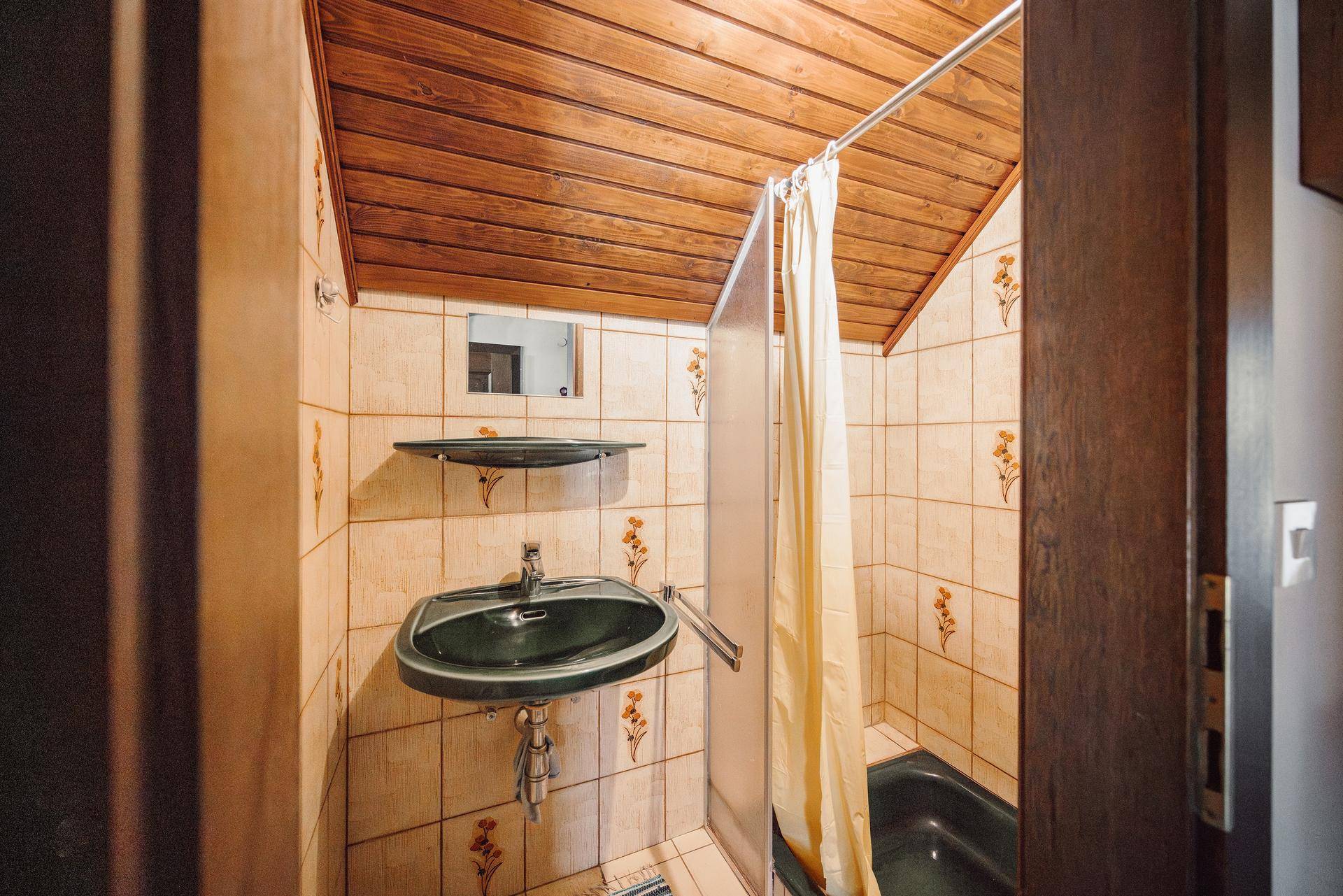 Badezimmer mit Dusche, Waschbecken und gefliesten Wänden im traditionellen Stil der 80er Jahre.