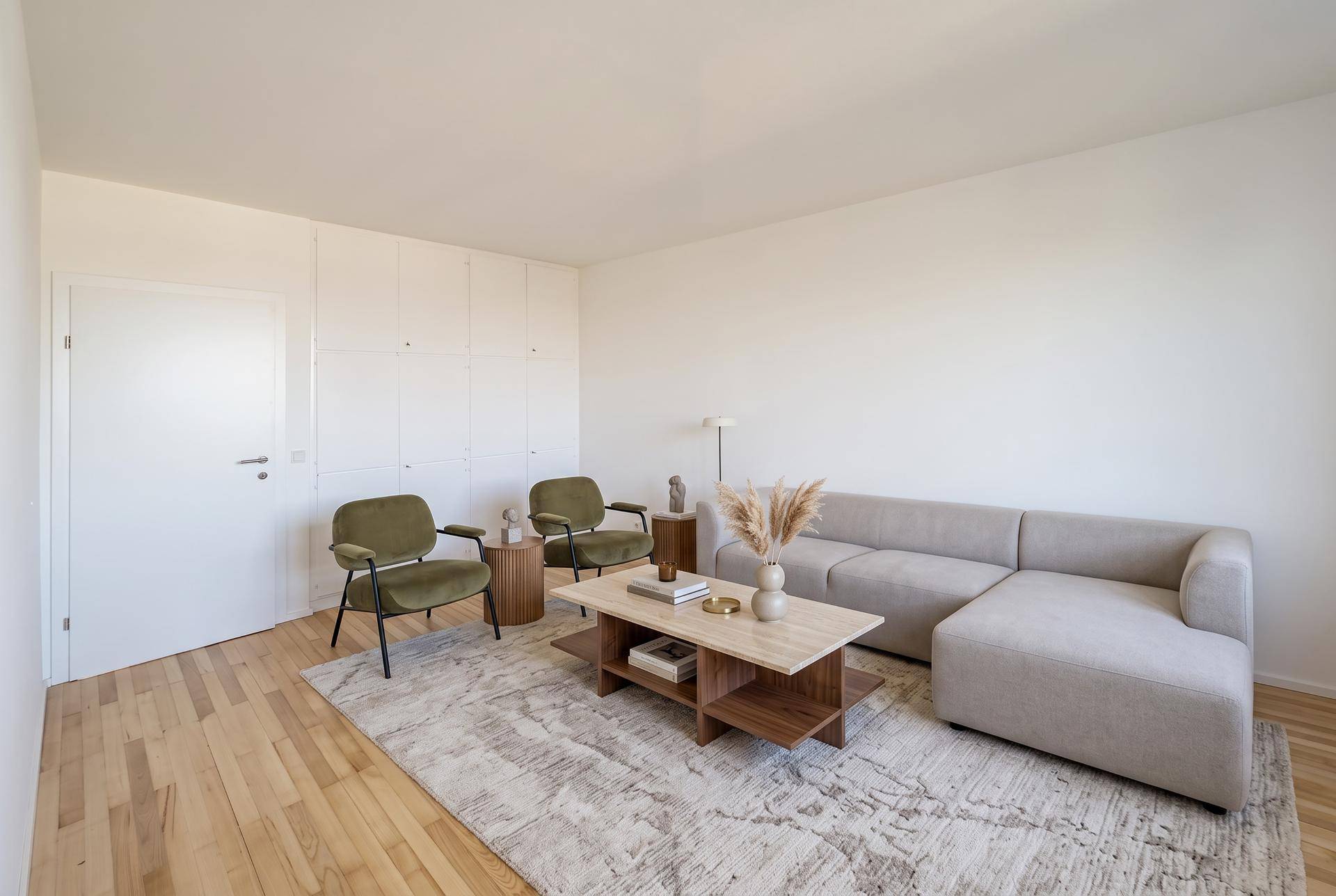 Helles Wohnzimmer mit beigem Ecksofa, zwei grünen Sesseln und integrierten Wandschränken.