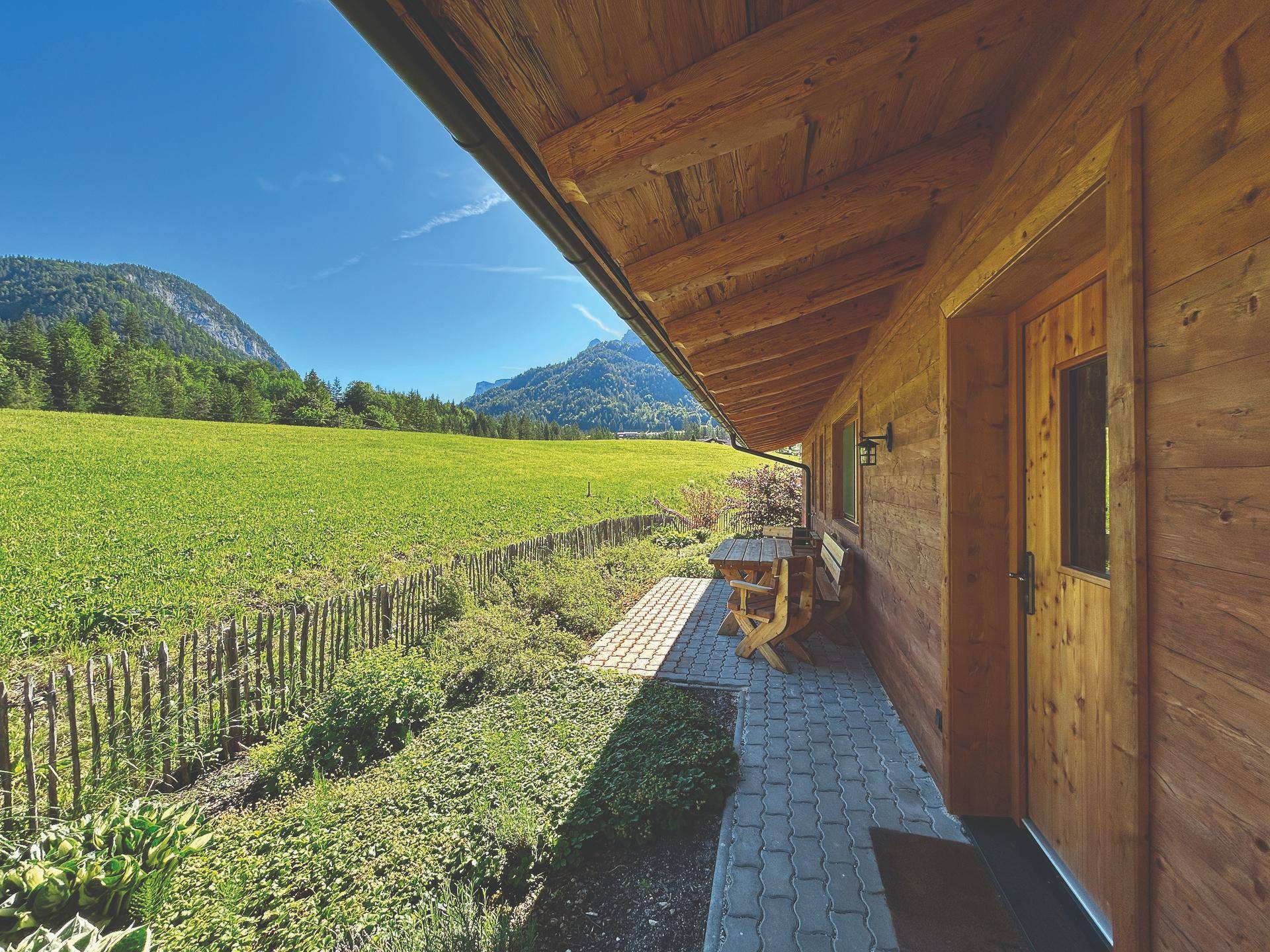 Charmantes Holzhaus mit gepflastertem Weg und Sitzgelegenheit inmitten grüner Natur.