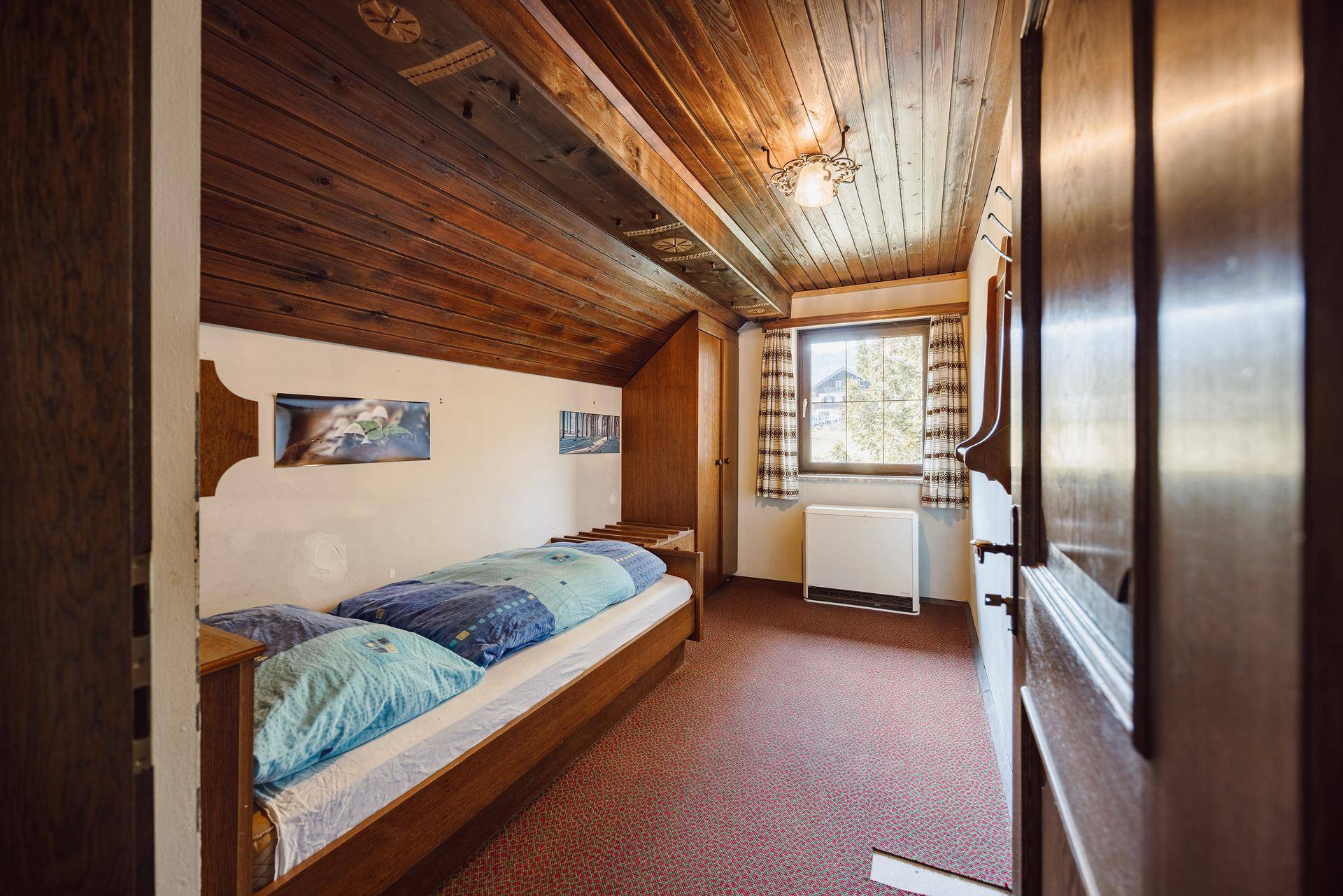 Gemütliches Schlafzimmer mit Holzbalkendecke, Einzelbett und Teppichboden unter Dachschräge.