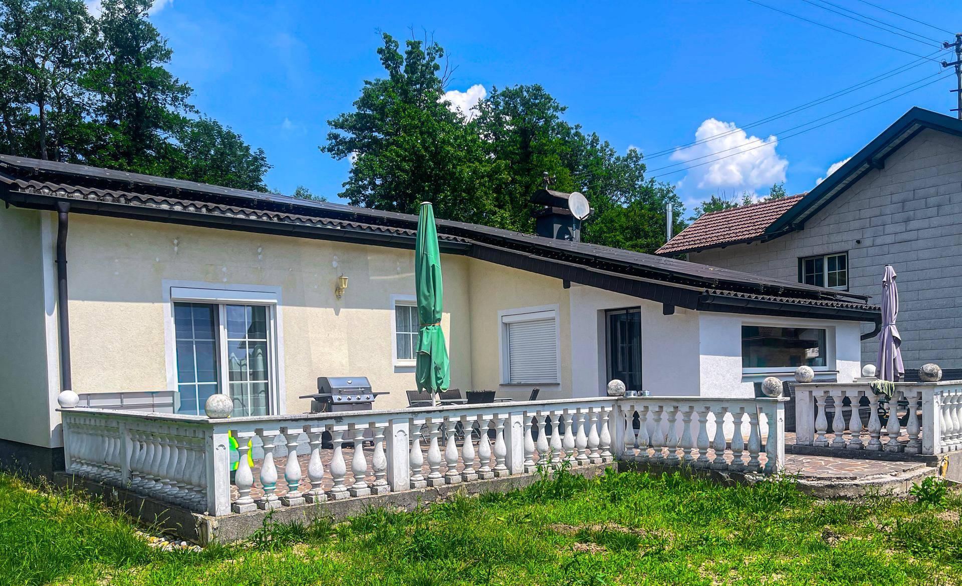 Großzügige Terrasse mit Grillbereich und Sonnenschirm, angrenzend an einen Garten.