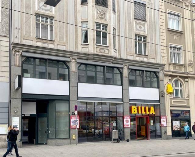 Fassade eines Geschäftsgebäudes mit Supermarkt im Erdgeschoss und traditioneller Architektur in den oberen Etagen.