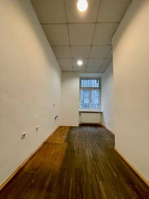 Schmaler Büroraum mit Holzfußboden, weiß gestrichenen Wänden und einem Fenster.