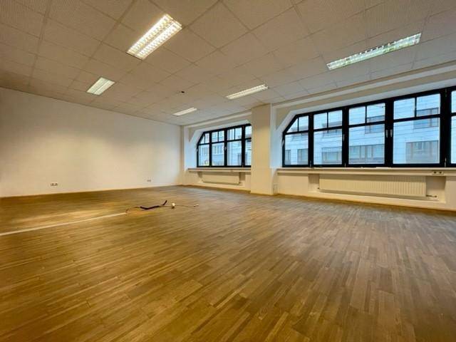 Heller Büroraum mit zwei großen Fenstern, Holzfußboden und abgehängter Decke.