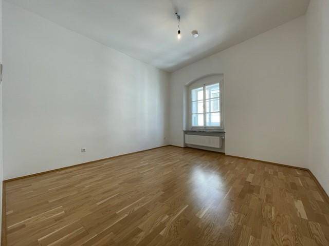 Helles Zimmer mit Holzboden und einem großen Fenster, das eine angenehme Atmosphäre schafft.