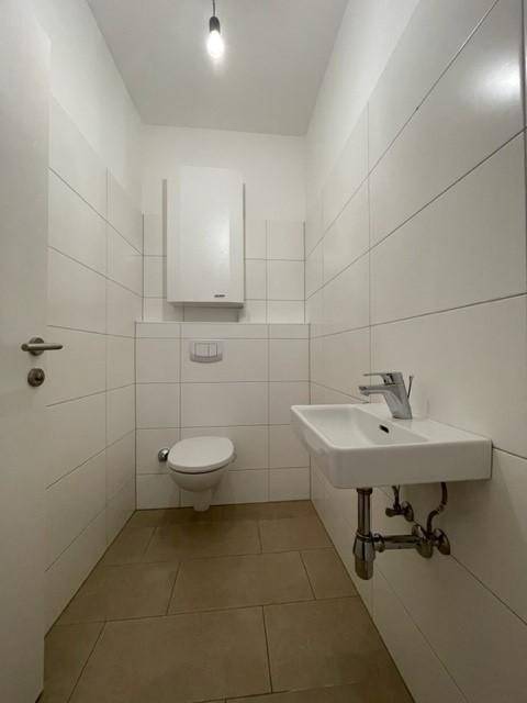 Kleines Gäste-WC mit Wand-WC, Waschbecken und weißen Fliesen an den Wänden.
