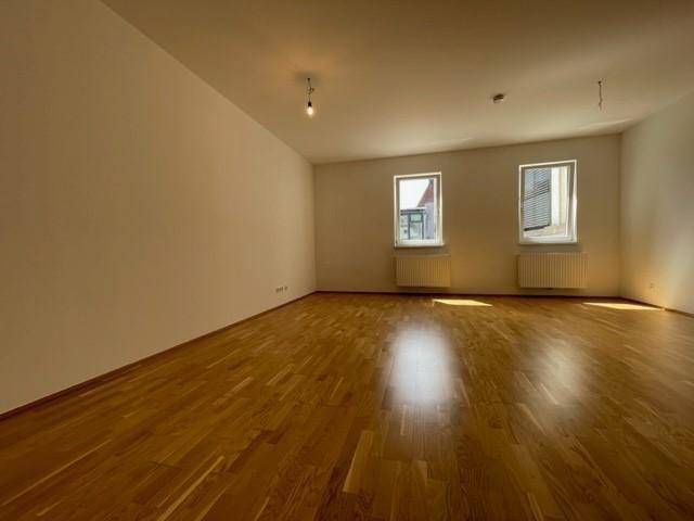 Geräumiger Raum mit Holzboden und zwei Fenstern, die viel Tageslicht hereinlassen.