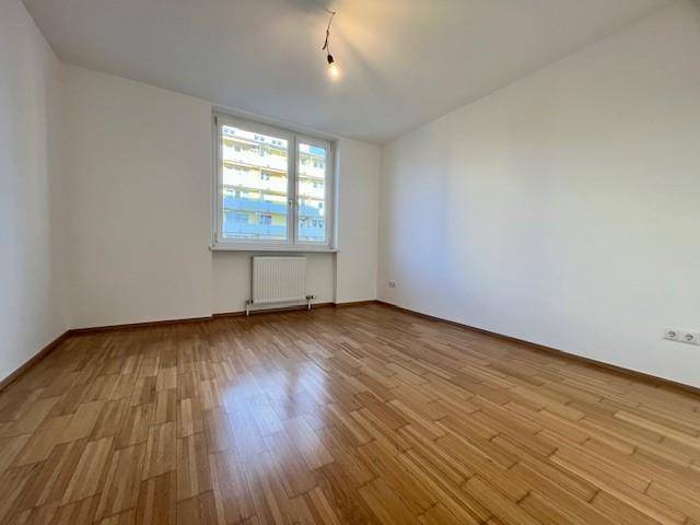 Geräumiges Zimmer mit hellem Parkettboden und einem großen Fenster, ideal als Schlaf- oder Wohnzimmer.