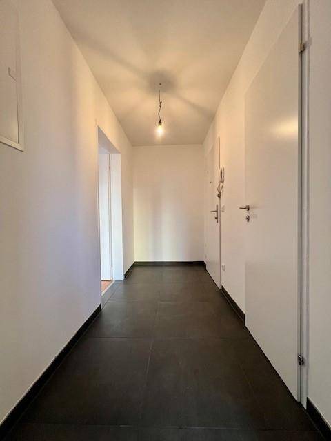 Langer, heller Flur mit dunklem Fliesenboden, der zu verschiedenen Räumen der Wohnung führt.