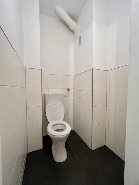 Separates WC mit weißer Toilette und halbhohen Fliesen, funktional und in gepflegtem Zustand.