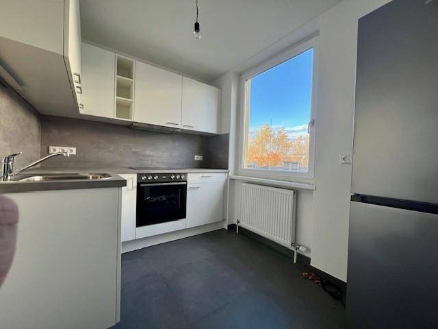 Funktionale Küche mit weißen Schränken, dunklem Fliesenspiegel und einem Fenster mit Blick nach draußen.