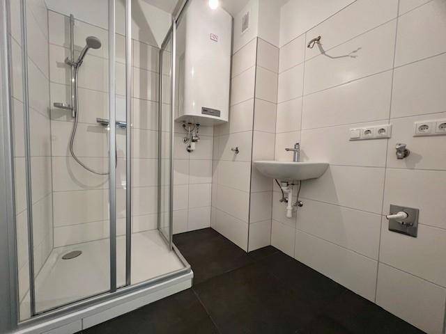 Modern gefliestes Badezimmer mit Duschkabine, Waschbecken und Boiler, in gutem und sauberem Zustand.