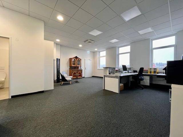 Großzügiger Bürobereich mit Teppichboden, Arbeitsplätzen und einem Blick in einen angrenzenden Sanitärraum.