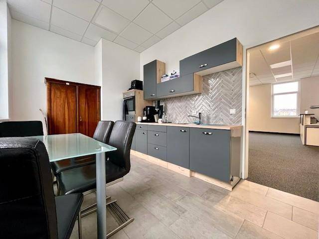 Moderne Teeküche mit grauen Schränken, Holztheke und Essbereich, ausgestattet mit Fliesenboden und Geräten.