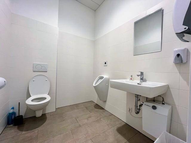 Sauberes und funktionales Badezimmer mit WC, Urinal, Waschbecken und Fliesen an Wänden und Boden.