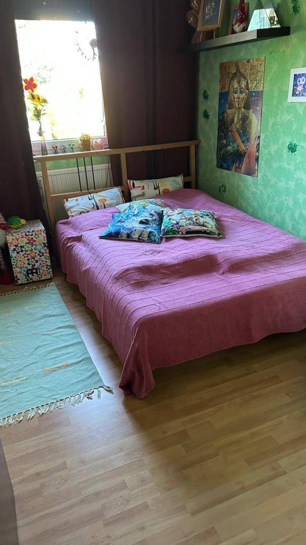 Helles Schlafzimmer mit Holzbett, lila Bettdecke und einer auffälligen grünen Wandgestaltung.