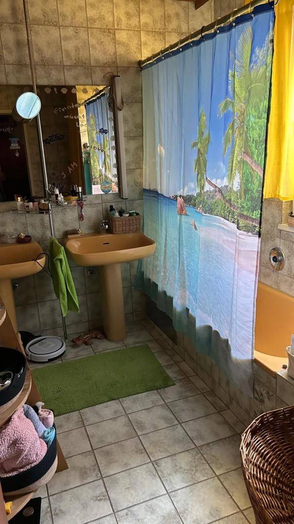 Badezimmer mit Fliesenboden, zwei separaten Waschbecken und einer Dusche mit tropischem Vorhang.