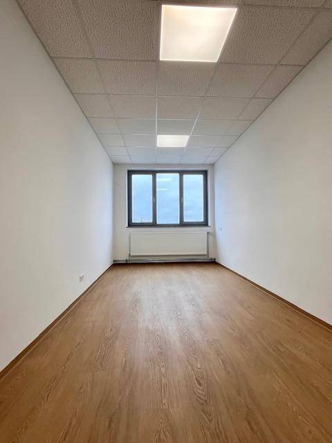 Leerer, schmaler Büroraum mit Fensterfront, hellem Boden und weißen Wänden, bereit zur Nutzung.