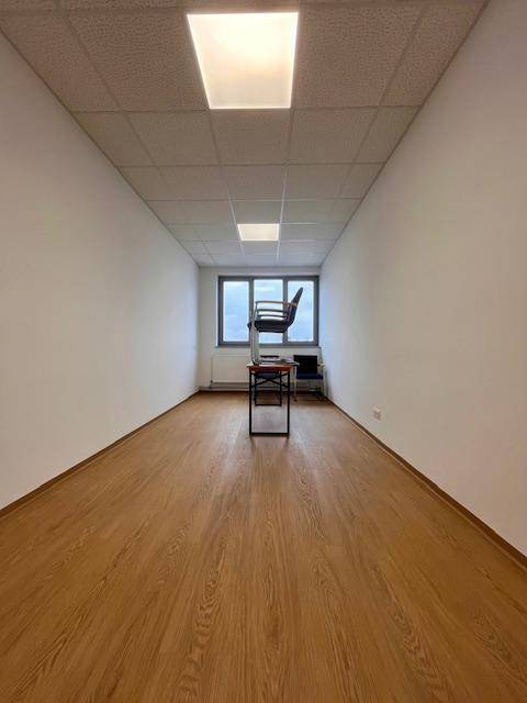 Langer, schmaler Raum mit Fenster am Ende, hellem Boden und minimalistischer Einrichtung.